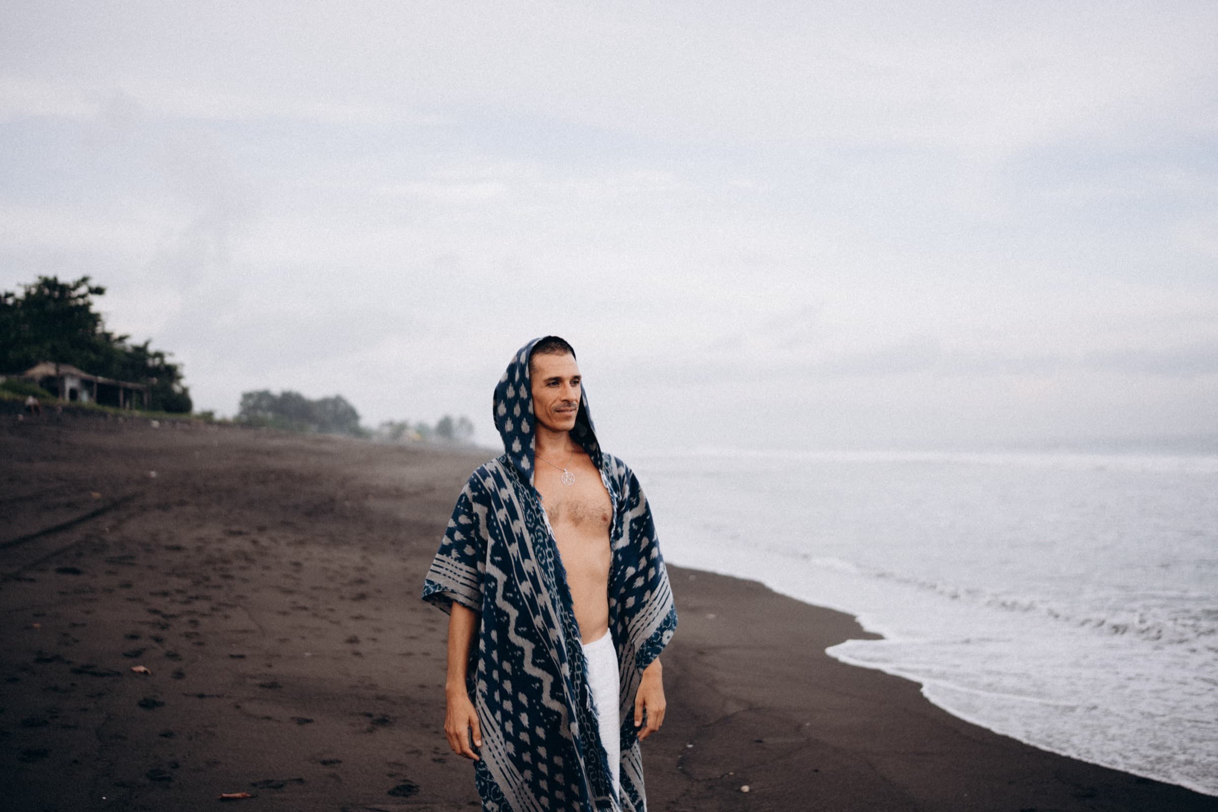 Mysticlio standing on a black sand shore at dawn as waves reach the sand