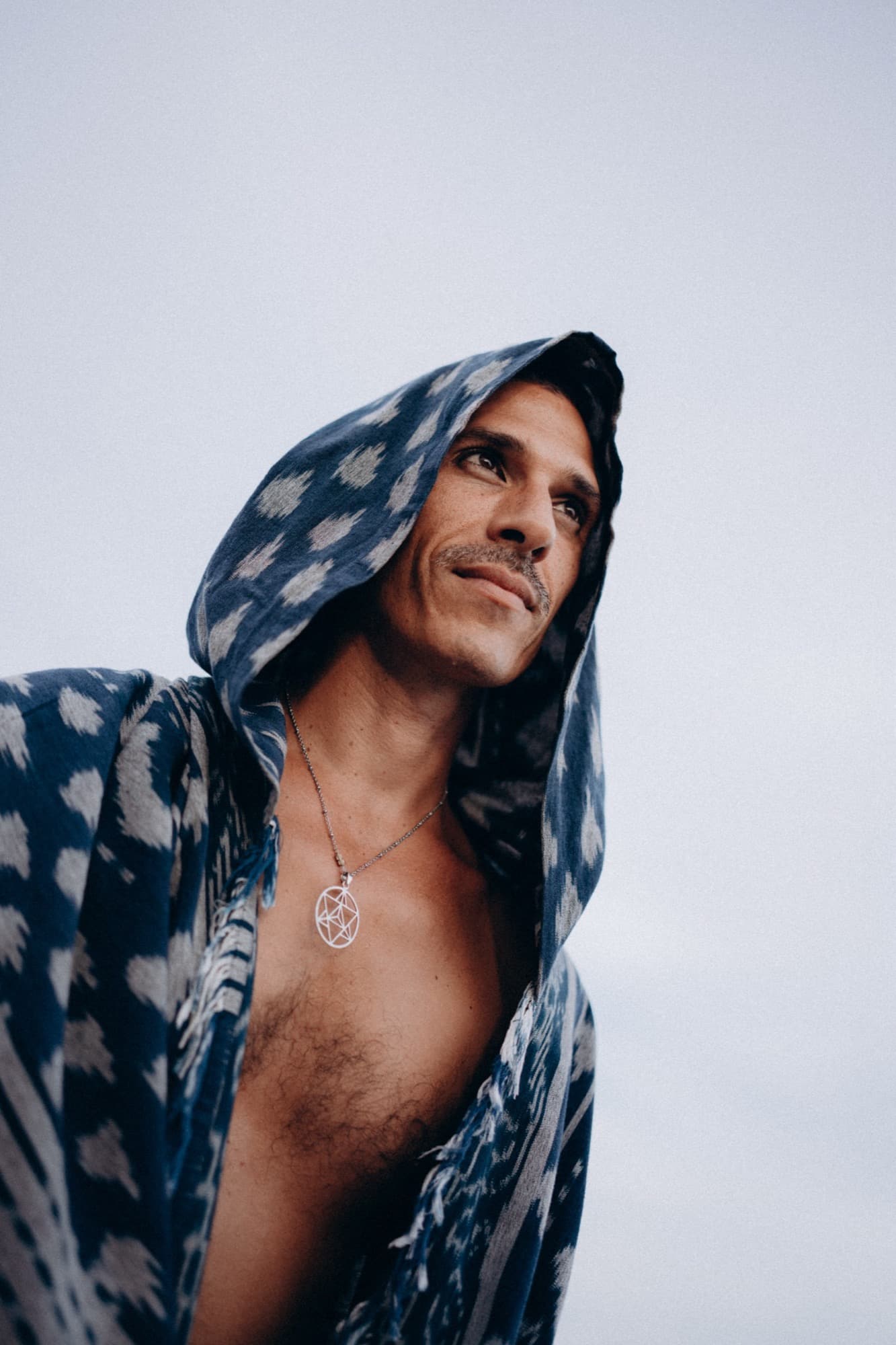 Mysticlio wearing a hooded indigo ikat shawl, looking up toward an open sky